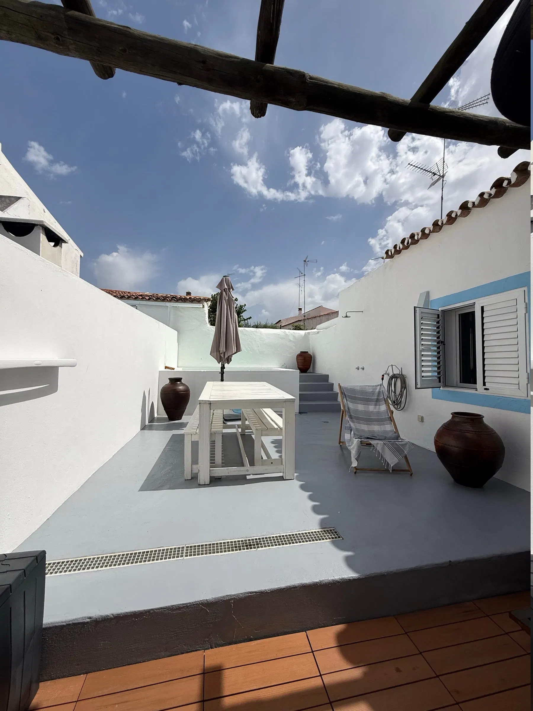 The courtyard from above — long and enclosed by whitewashed walls, with a table, a folded parasol and a clay urn.