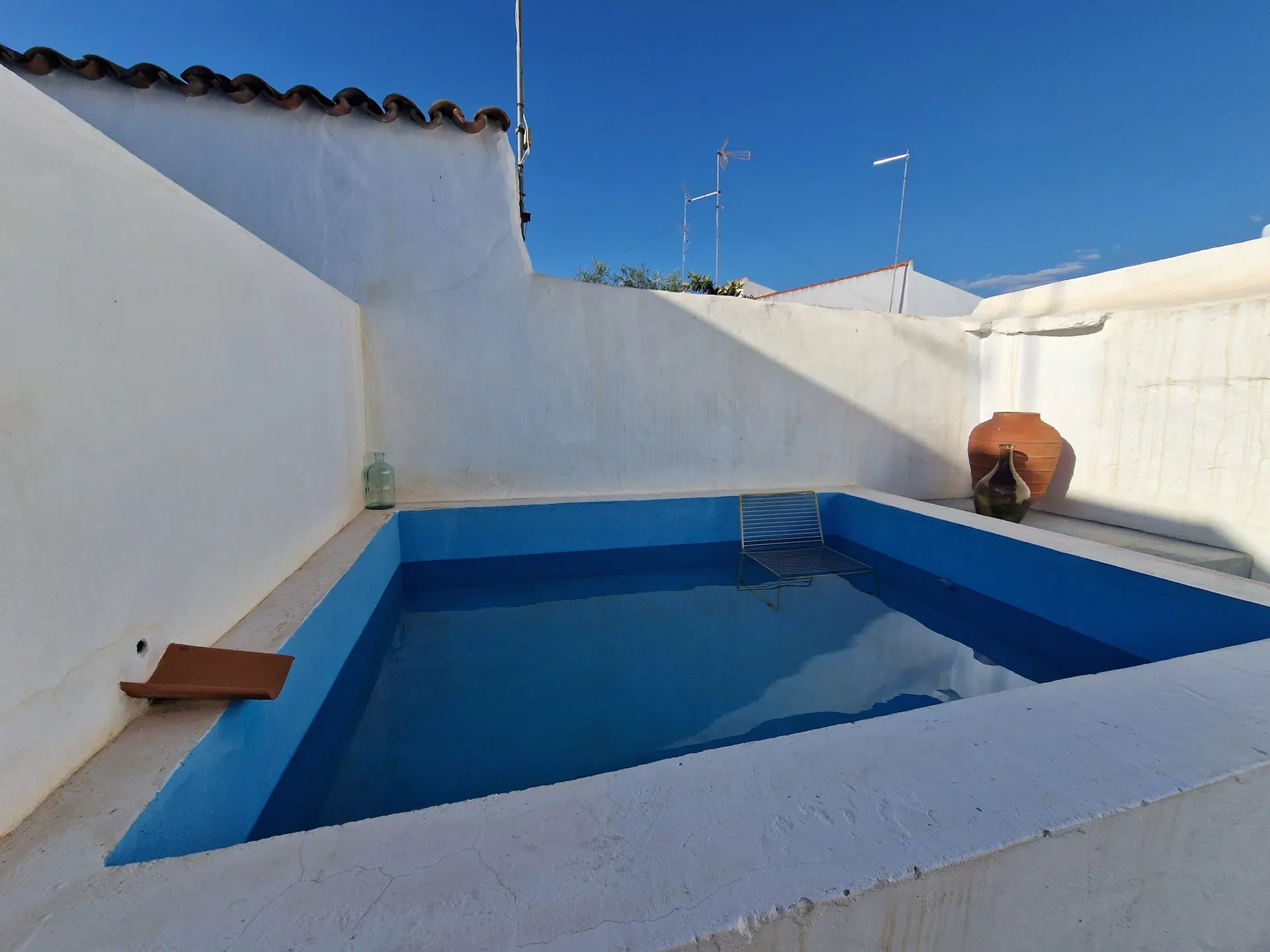 A piscina vista de perto, com o interior pintado de azul vivo e as paredes caiadas do pátio à volta.