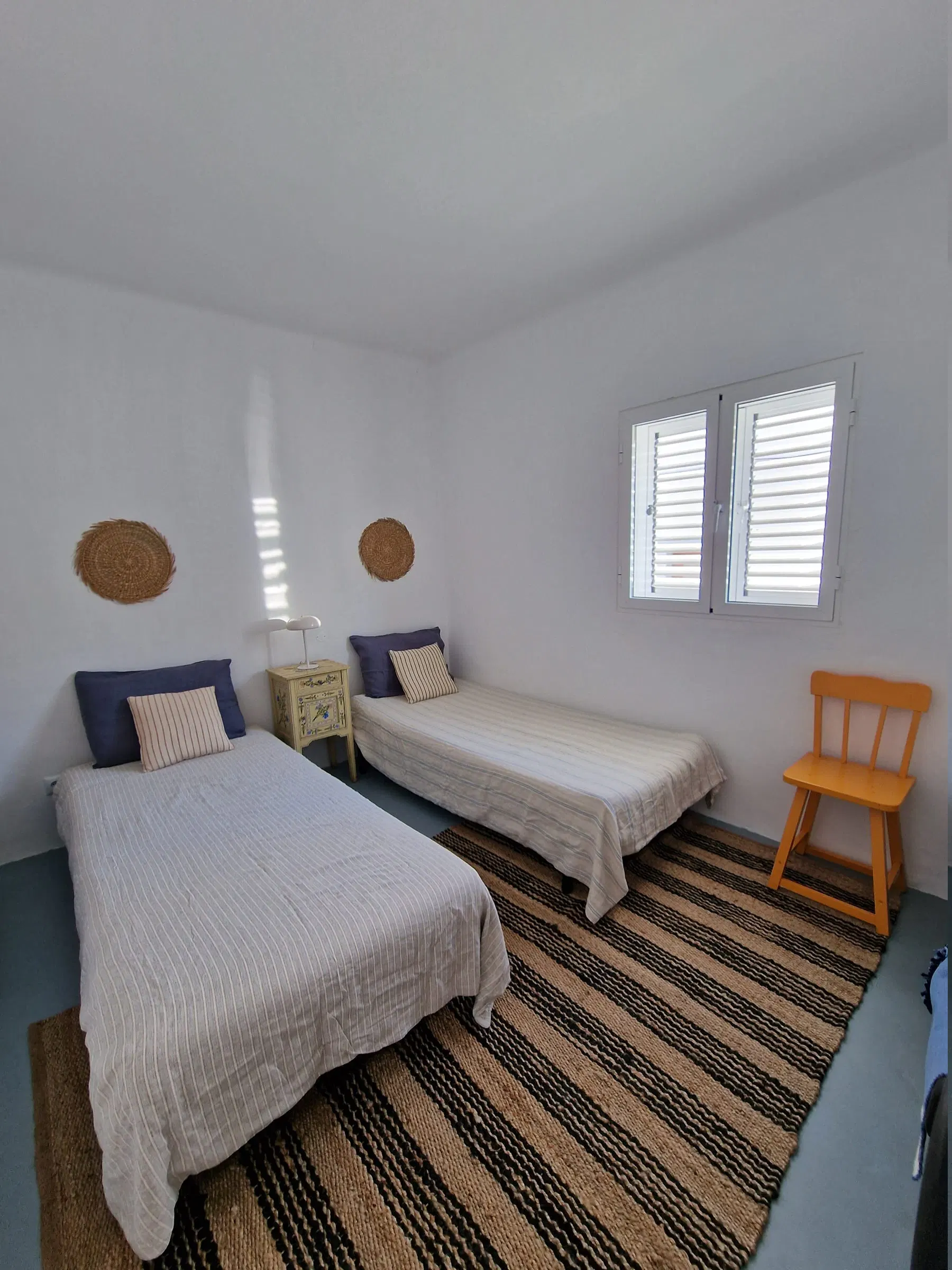 A twin bedroom with navy cushions, a striped rug and a wooden chair in the corner.