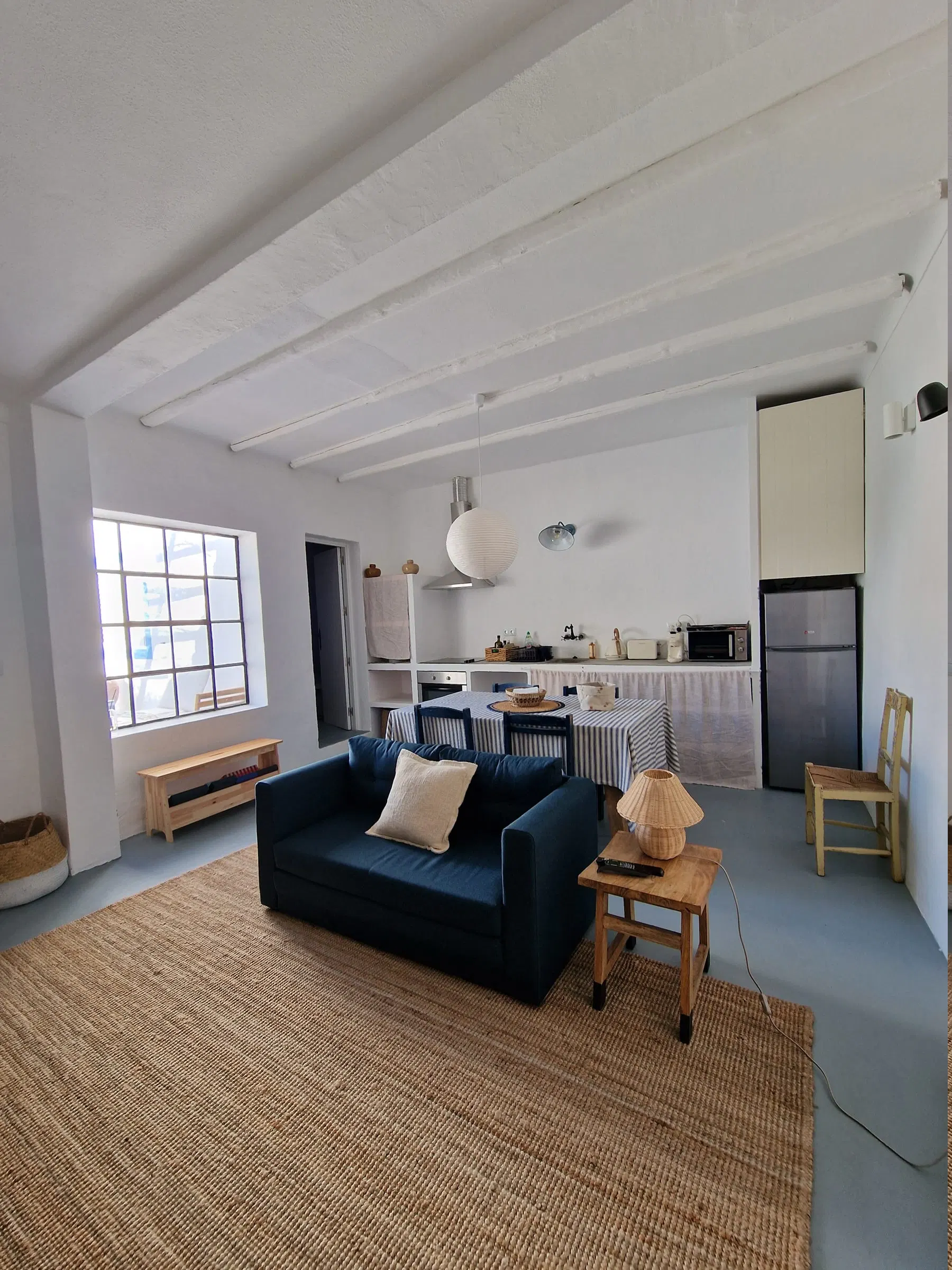 The living room open to the kitchen, with a navy sofa, dining table and a large black-framed window.