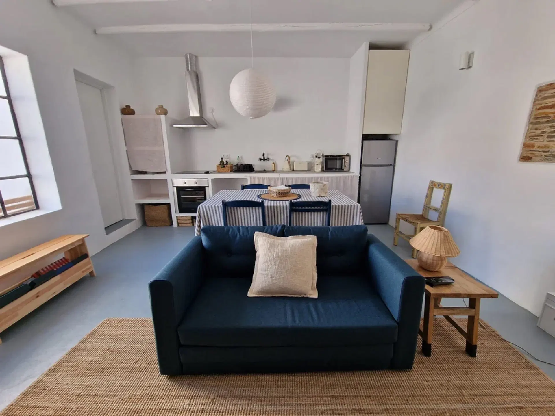 A navy sofa on a jute rug, the kitchen beyond, under a white beamed ceiling.