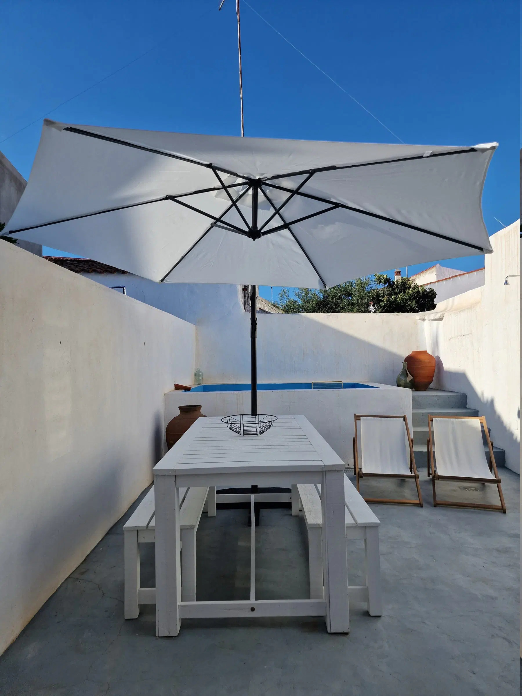 A white table laid in the shade of a large parasol on the house's terrace, the whitewashed wall behind.