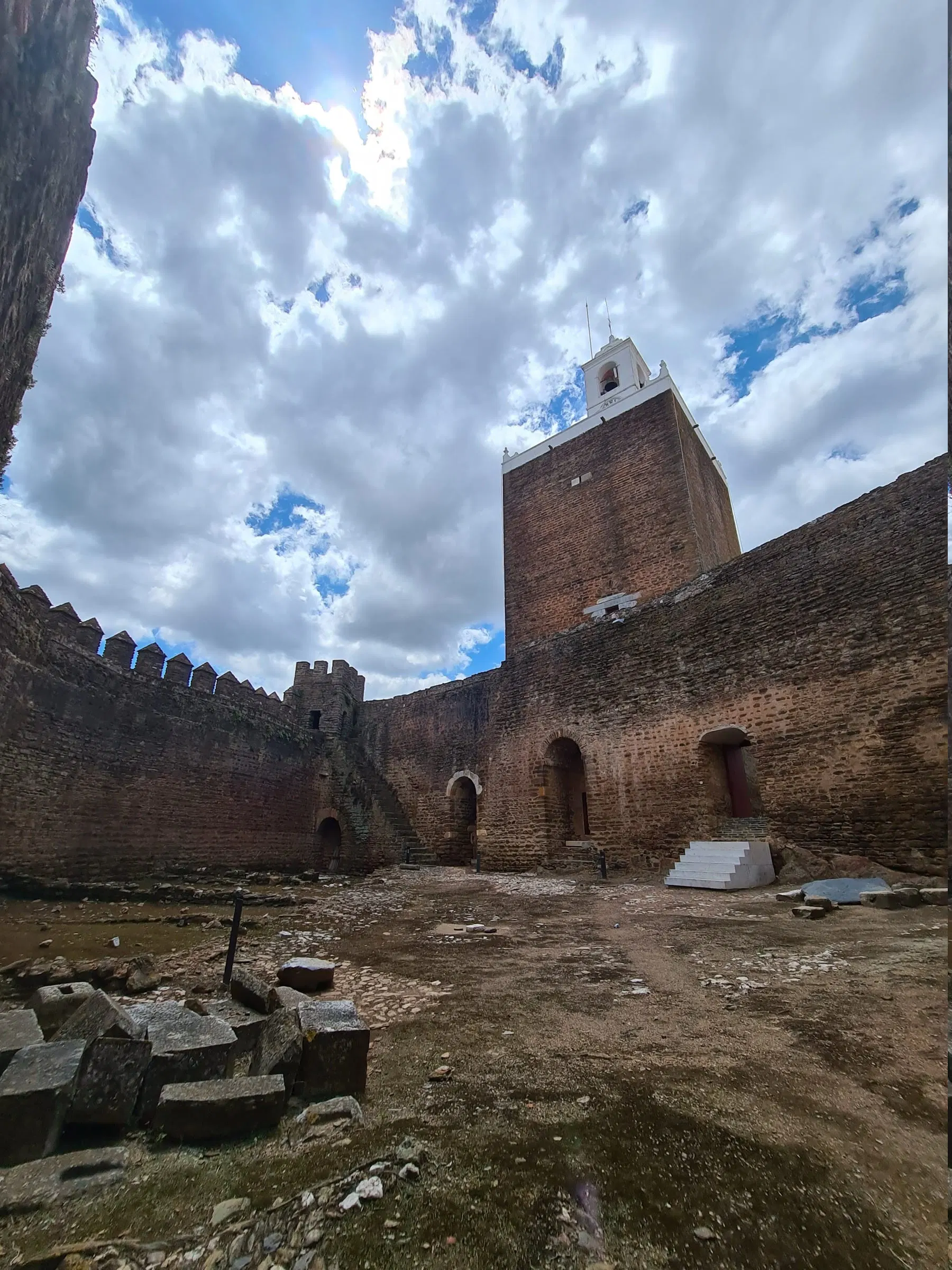 Muralla y torre del castillo de Alandroal, en piedra oscura, bajo un cielo nublado.