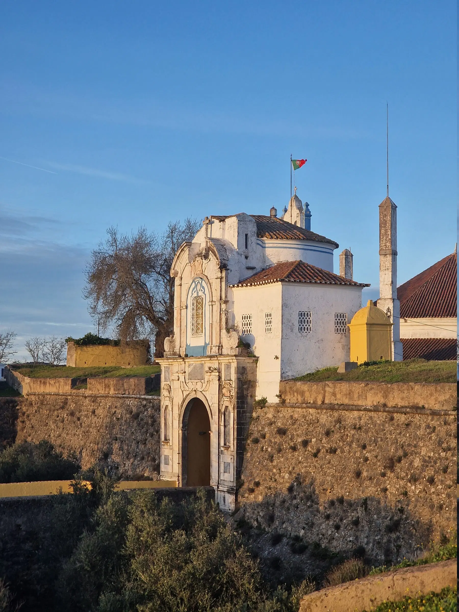 Ermida branca encavalitada na muralha de Elvas, com bandeira ao vento.