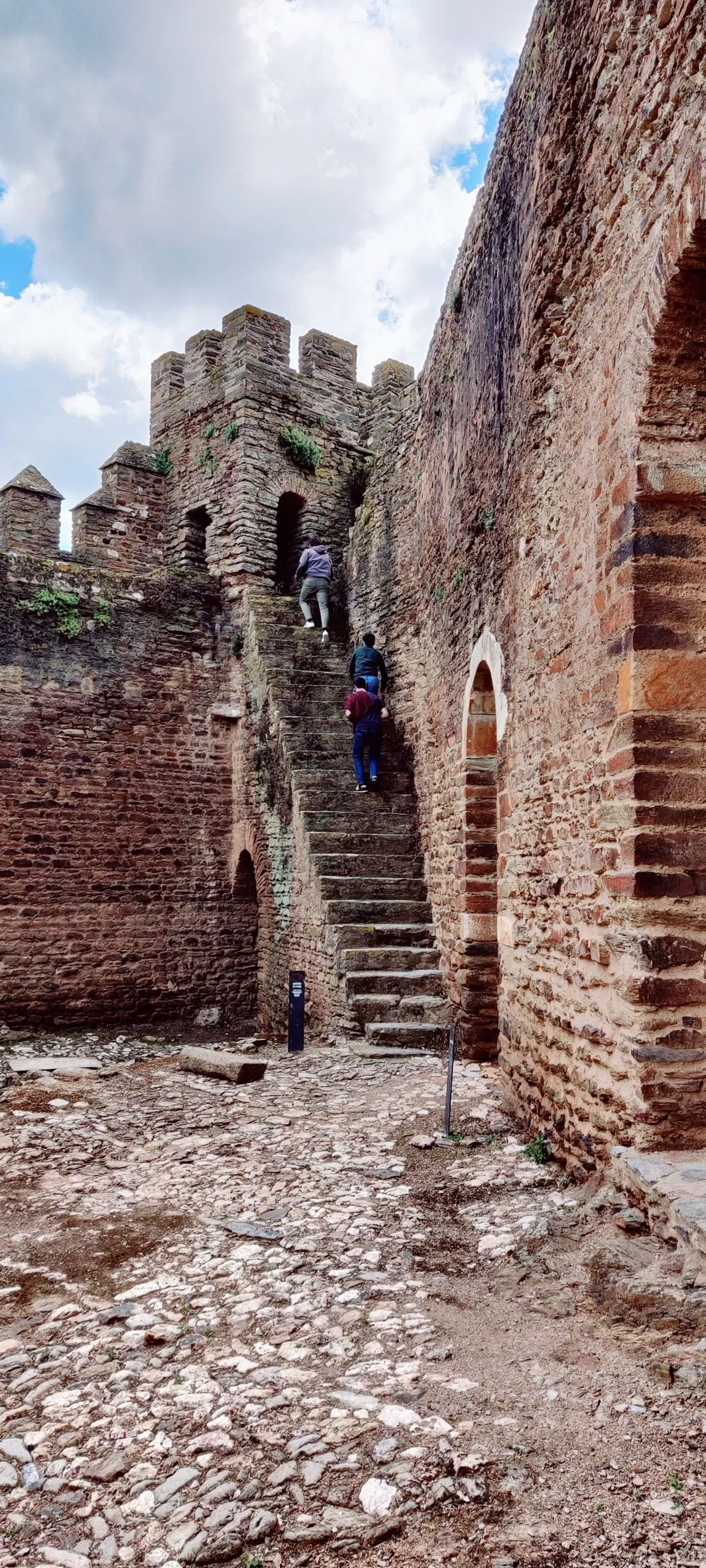 Escadaria de tijolo antiga a subir junto a uma muralha, com visitantes a meio.