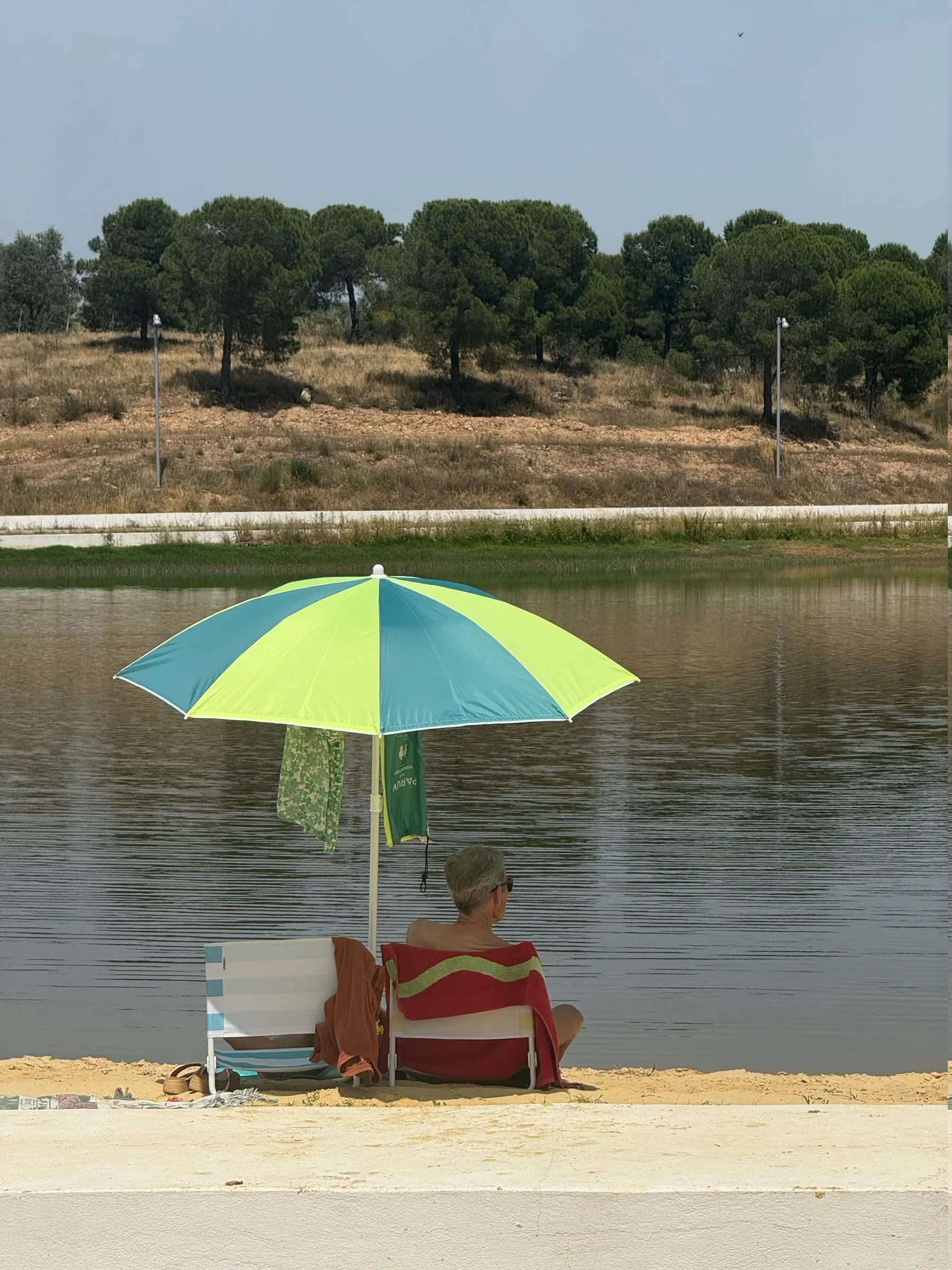 A brightly coloured parasol at the water's edge, woodland reflected in the reservoir.