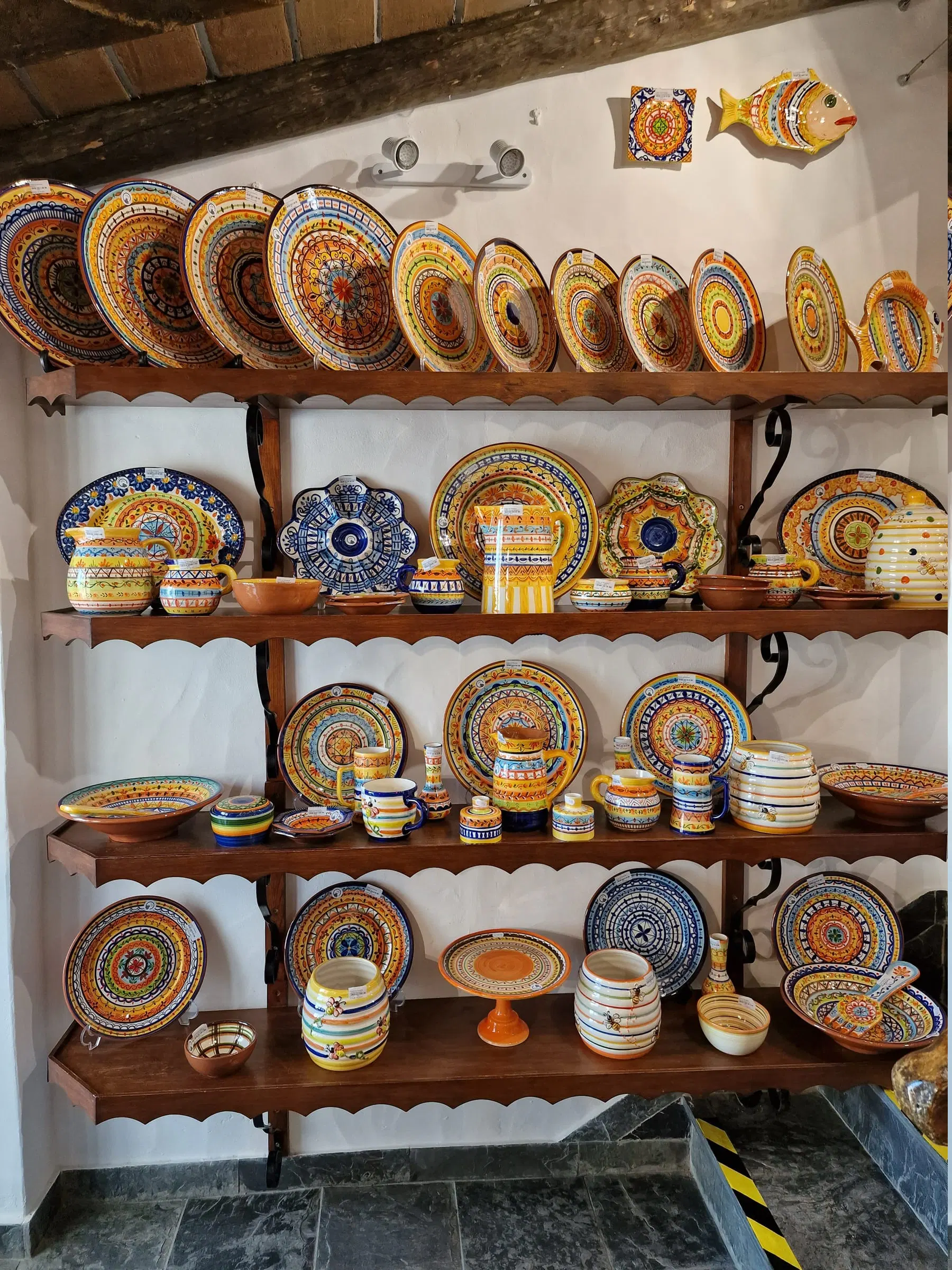 Prateleiras de louça pintada à mão numa loja de artesanato em Monsaraz — pratos, taças e jarros de barro.