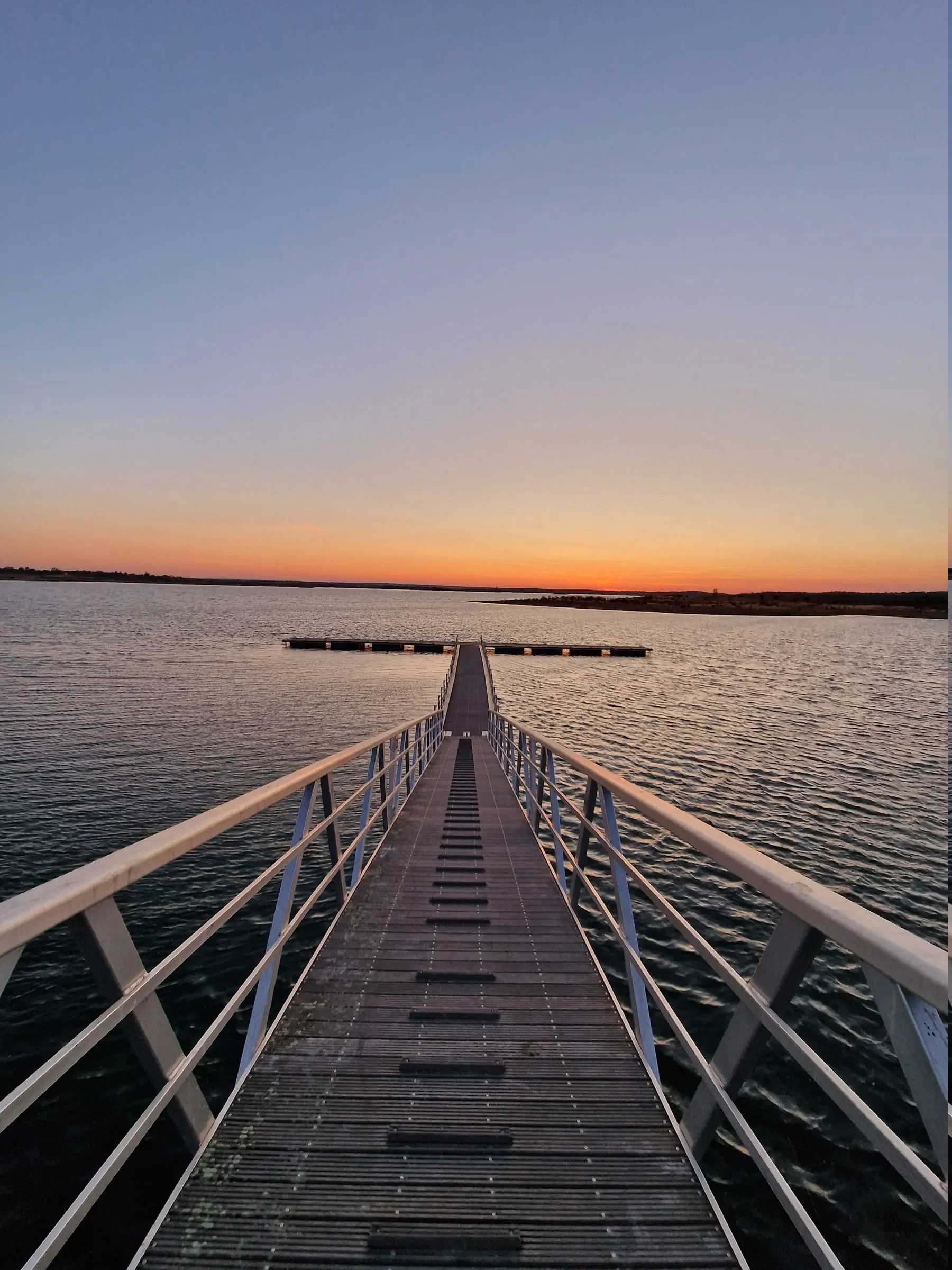 The boardwalk at water level, reaching out over the reservoir to the horizon at dusk.
