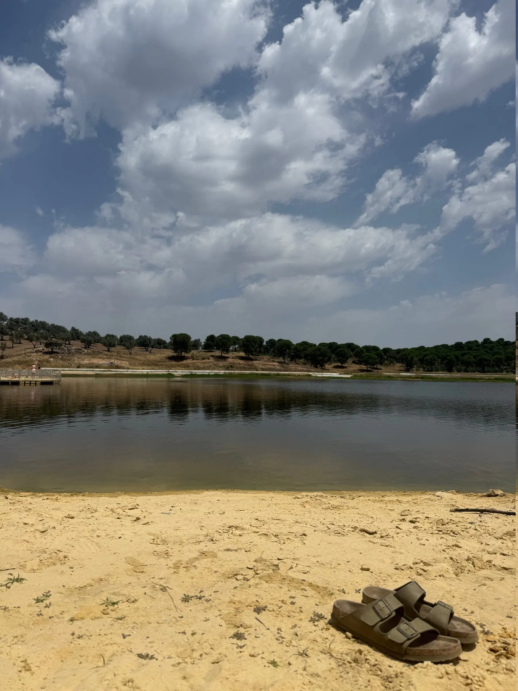 A Praia Fluvial do Lago, em Moura, com a mata da margem oposta reflectida na água parada.