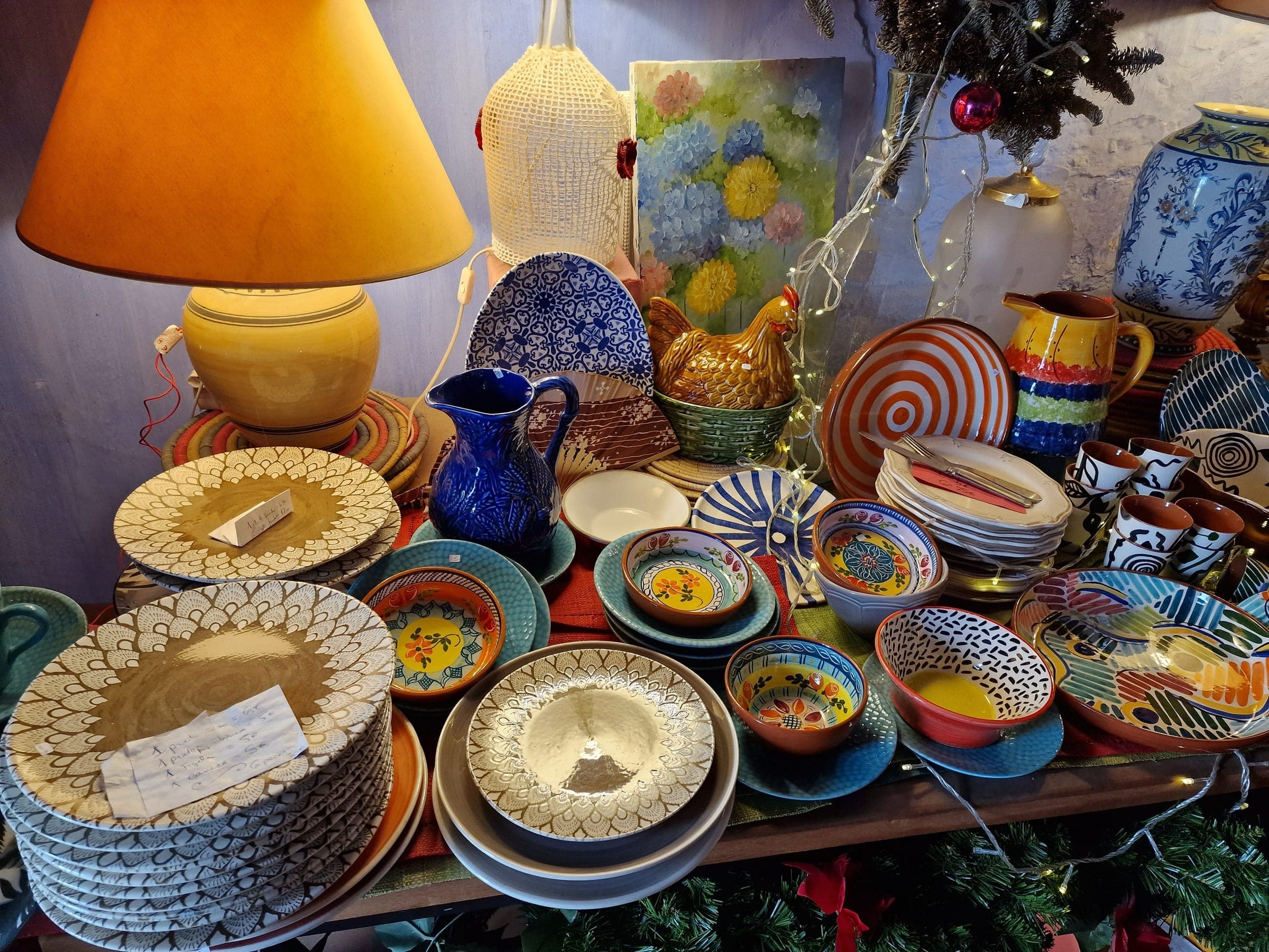 Mesa de artesanato com taças pintadas, cestos e candeeiros de palha.