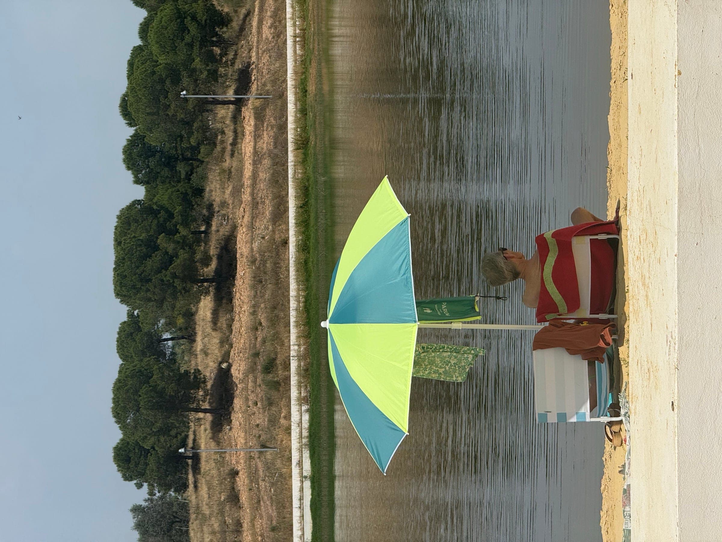 A brightly coloured parasol at the water's edge, woodland reflected in the reservoir.