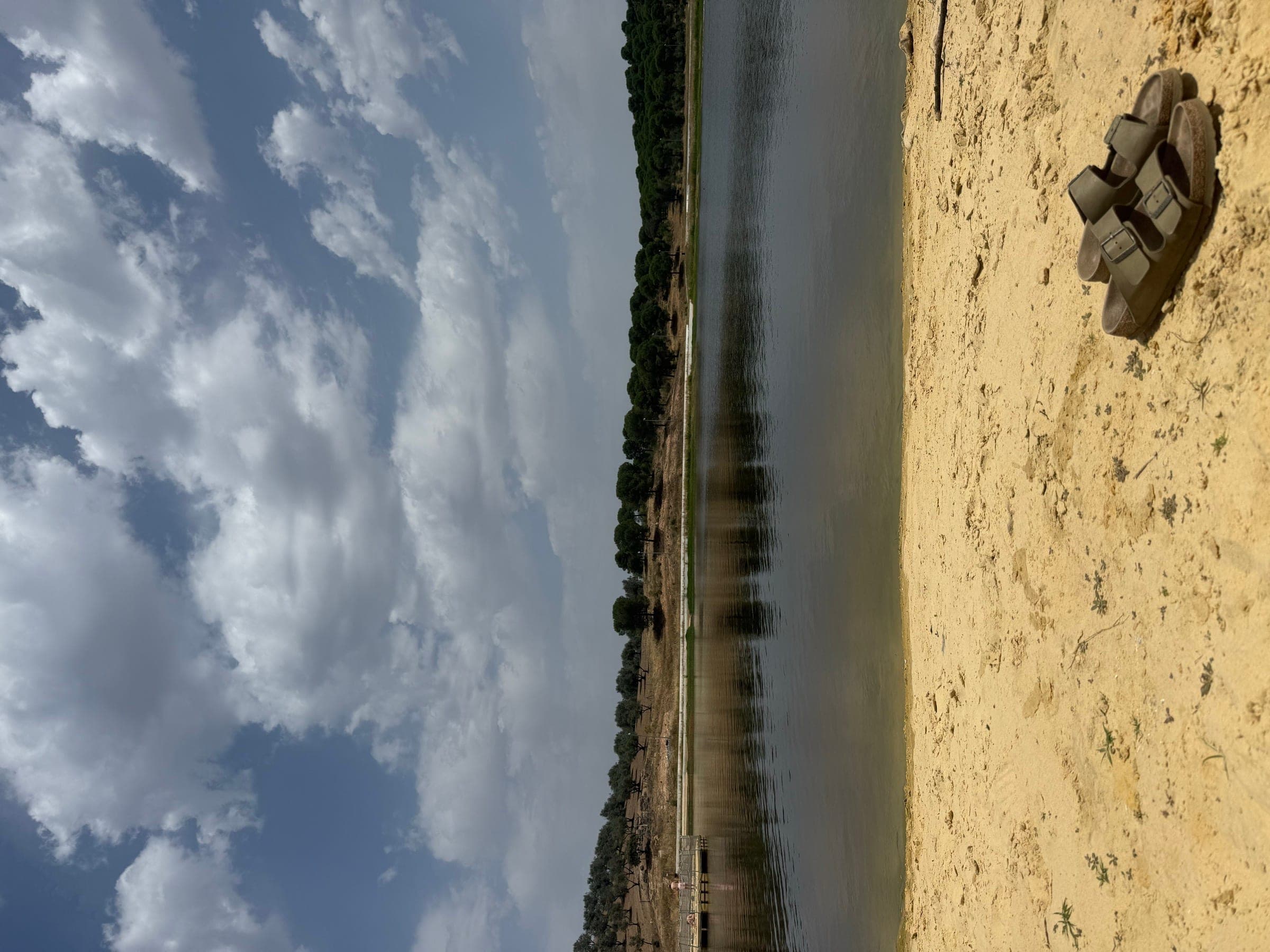 A Praia Fluvial do Lago, em Moura, com a mata da margem oposta reflectida na água parada.